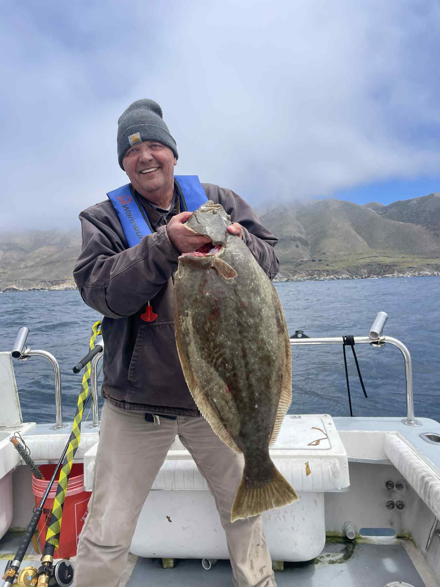 Veteran holding large halibut with coastal mountains behind